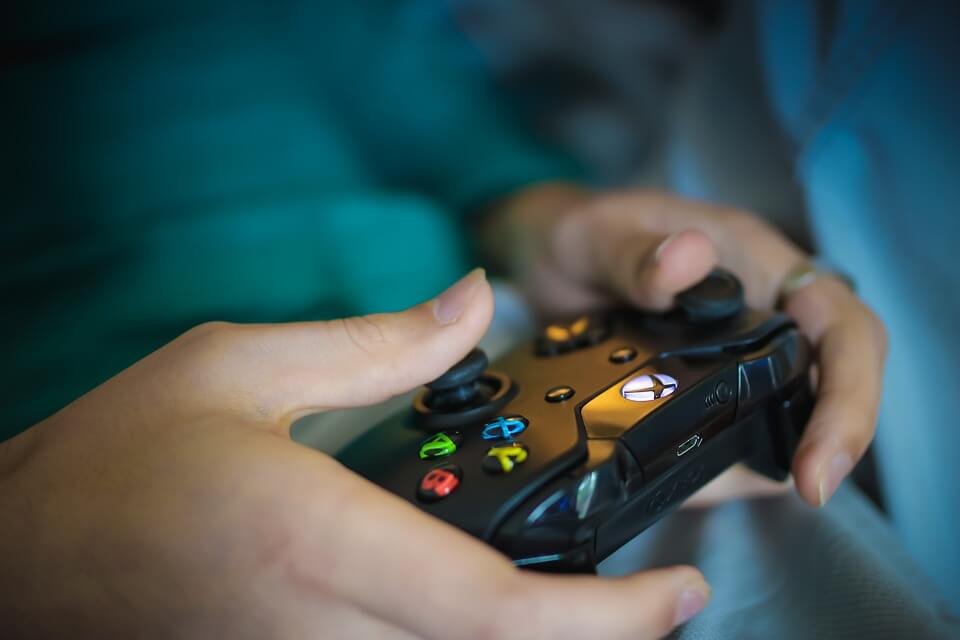 Close-up view of hands holding a black Xbox controller, thumbs resting on the analog sticks