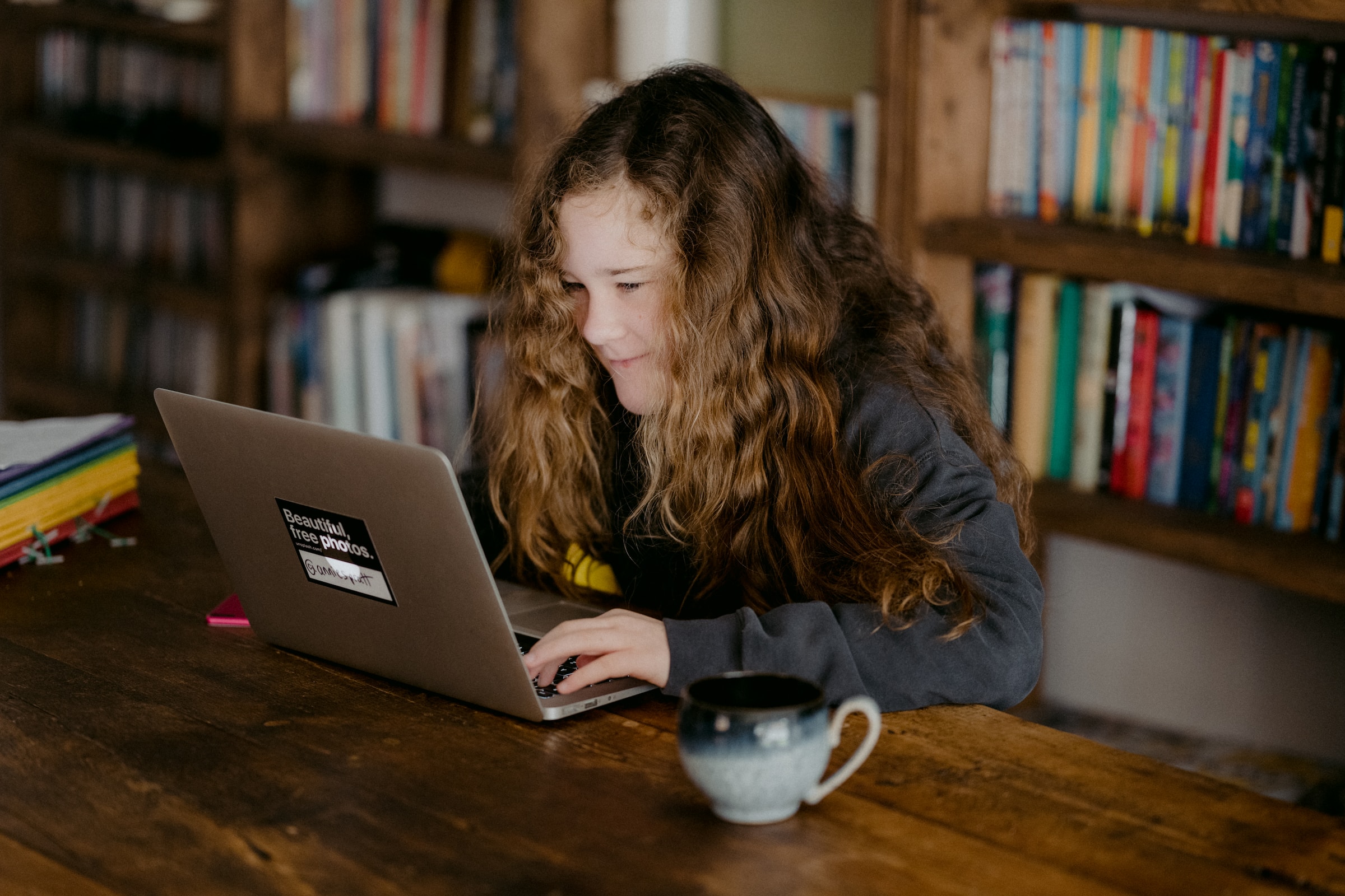 A girl with a slight smile on her face is sitting at a desk and using a laptop computer