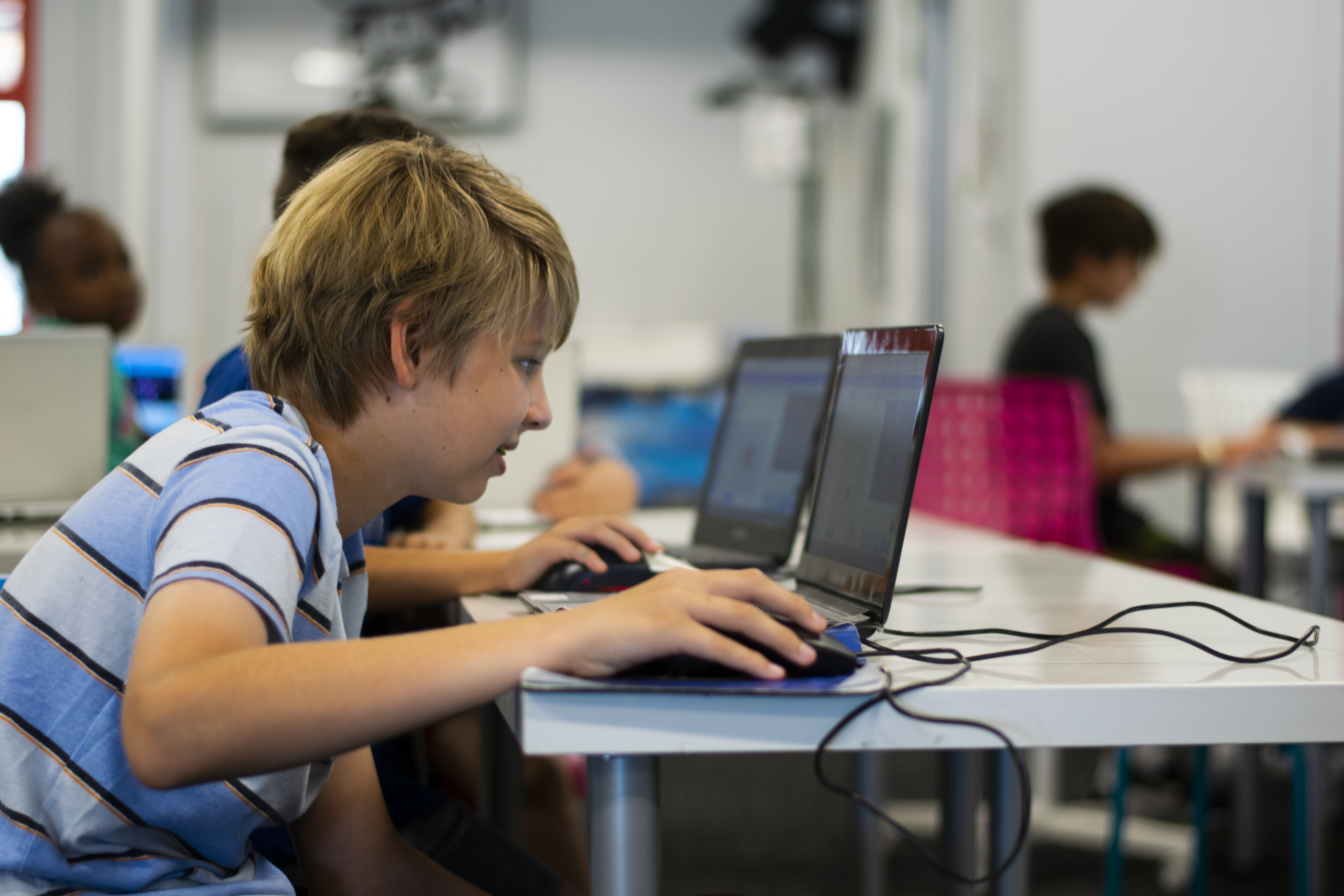 A boy in a striped blue shirt staring at a laptop with focus