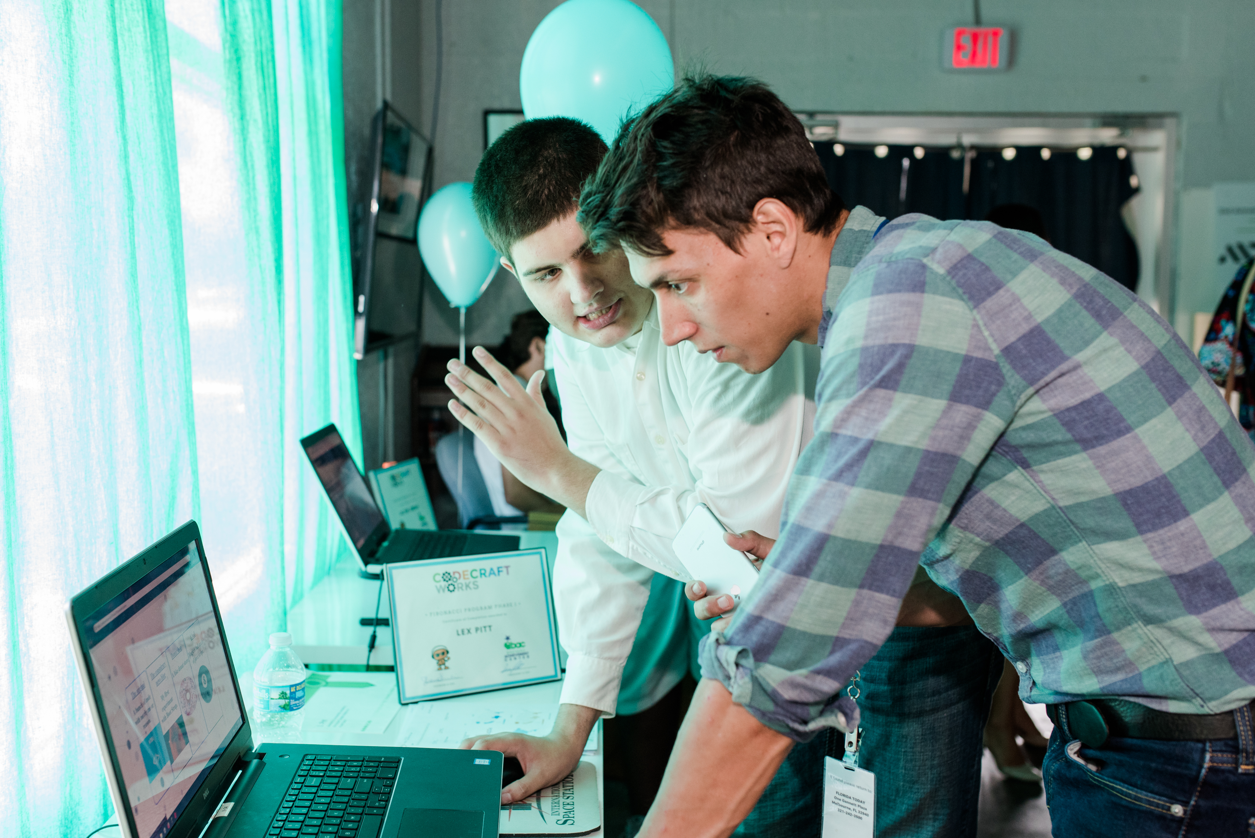 Two men, one in a white long-sleeve shirt and the other in a blue plaid shirt with the arms rolled up stare at a laptop
