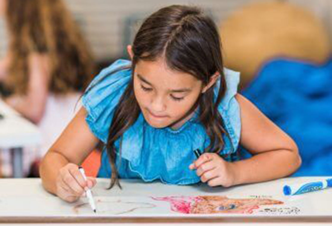 A girl in a blue shirt focused on drawing on a white surface