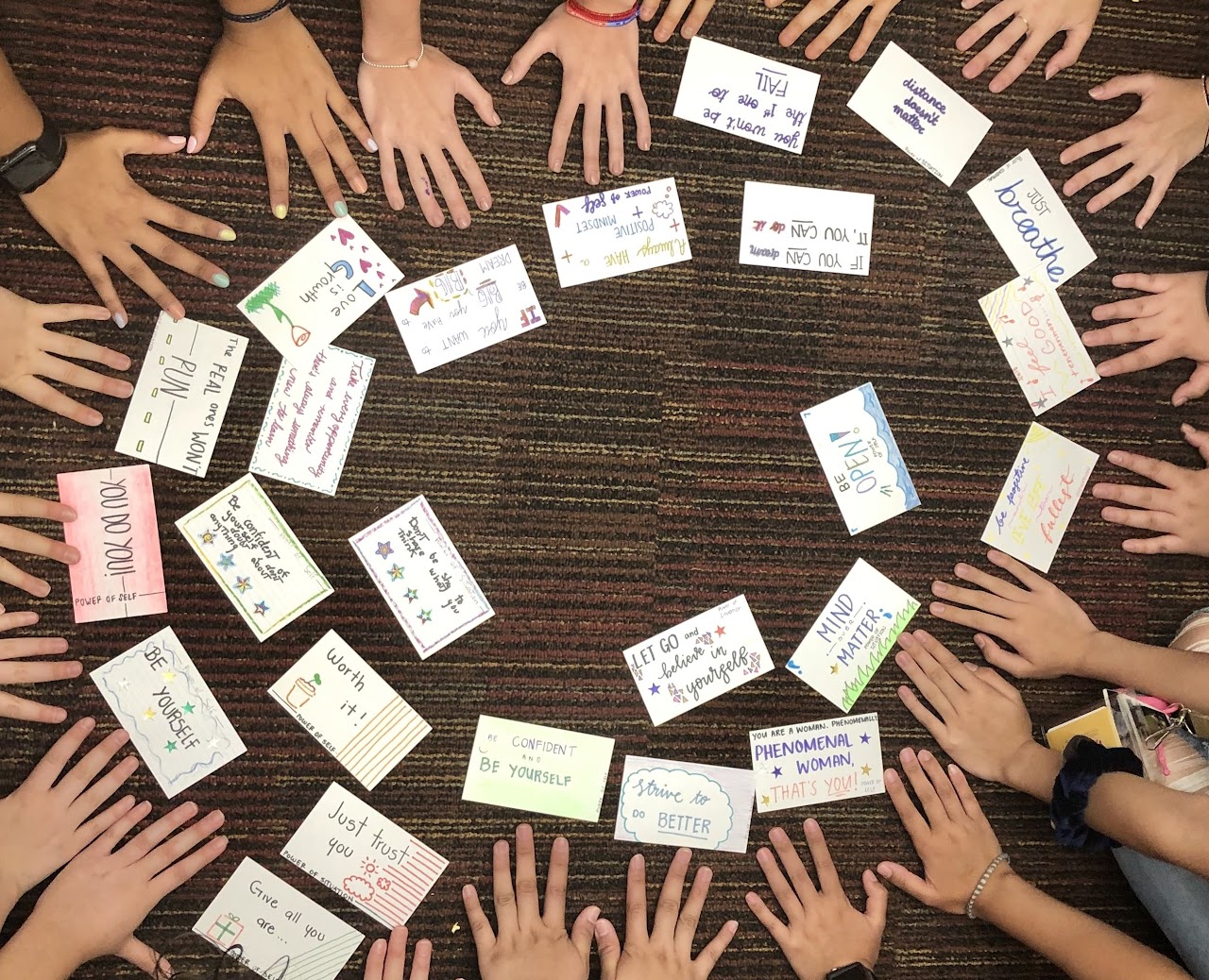 Several students hands in a cricle around some index cards with Mantras written on them